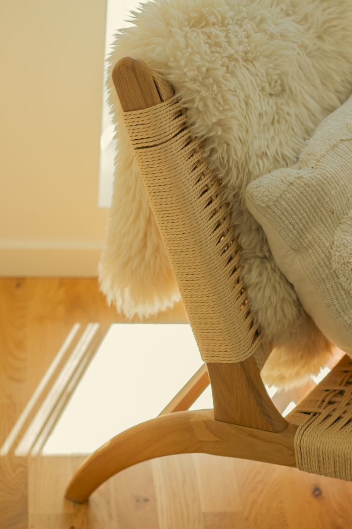 Warm sunlight on a wooden woven chair with textiles in a minimalist setting.