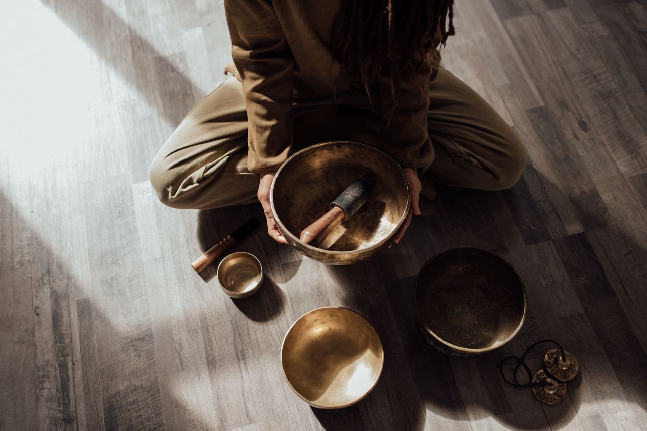 A woman engaging in a meditative sound bath using Tibetan singing bowls on a wooden floor.